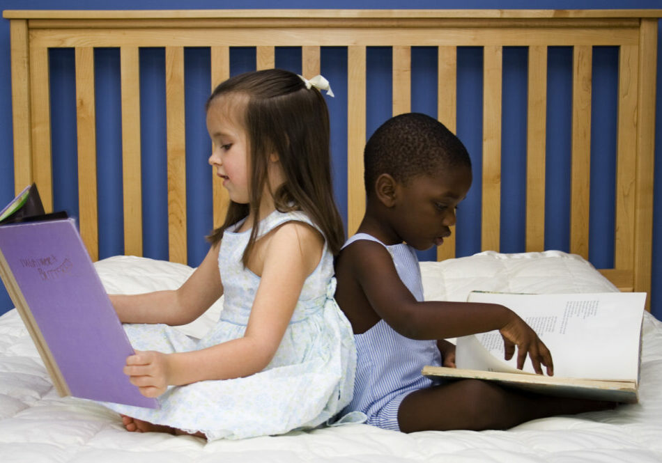 Two small children reading together on a bed.